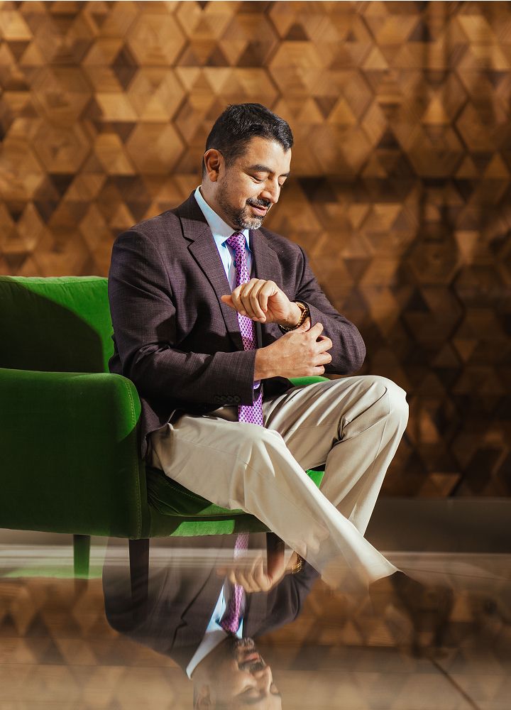 Best St. Louis Facial plastic surgeon, Dr. Nayak checking watch while sitting on green couch.