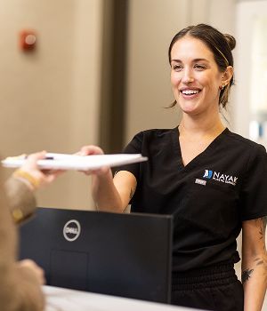 Smiling receptionist at Nayak Plastic Surgery handing paperwork to client.