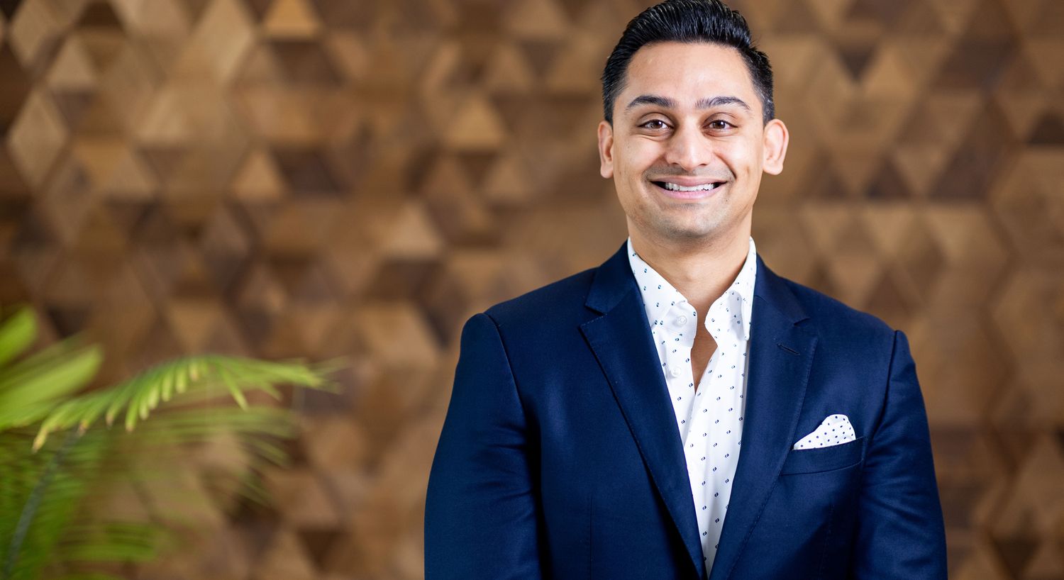 Smiling man in formal attire against wooden background.